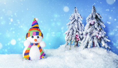 A toy snowman in the snow with Christmas trees on a blue background