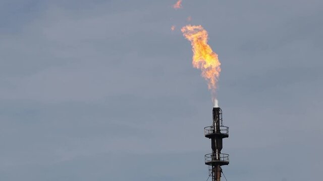 a large flame of fire emerging from an industrial chimney at a refinery plant
