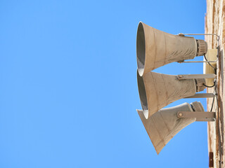 Three gray horn loudspeakers fixed on a stone wall on the right side of the image against a blue sky. Copy space. Selective focus.