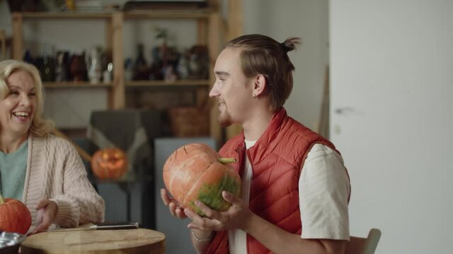 A man in front of a pumpkin for halloween from the table and shows it to his family