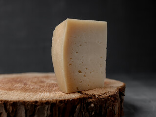 a piece of  cheese on a wooden stand on a dark background - 463319537