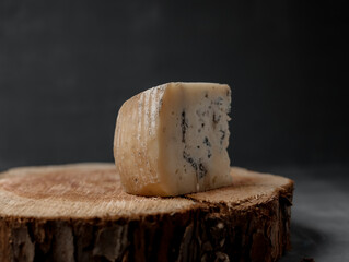 a piece of blue cheese on a wooden stand on a dark background - 463319546