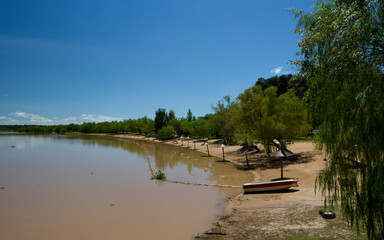 View of the river shore in a summer sunny day. A boat in the sand and the tropical jungle in the background reflected in the water.