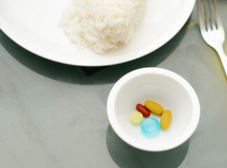 Tablets in a container for medicinal and dietary supplements, on the table, with rice in a plate and a fork.