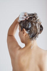Back view of senior woman with bare shoulders washing hair with shampoo