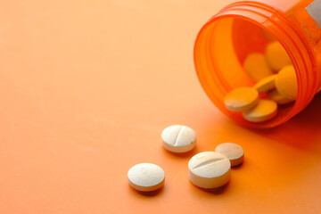  white color medical pills spilling on orange background 