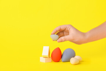 Female hand with stylish makeup sponges on color background