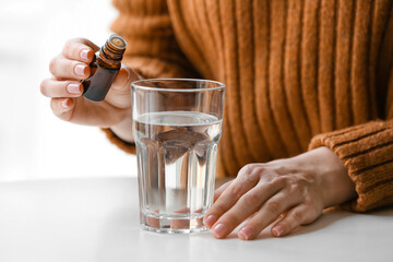 Woman adding essential oil to water in glass on table