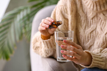 Woman adding essential oil to water in glass at home