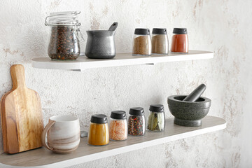 Jars with different spices, coffee beans and kitchen utensils on shelves