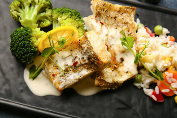 Plate with delicious baked cod fillet, rice and vegetables on color background, closeup