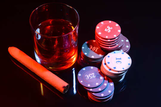 Poker chips, glass of beverage and cigar on dark background