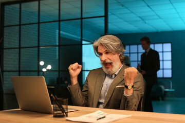 Happy mature businessman working with laptop in office at night