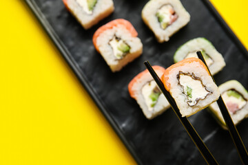 Chopsticks with delicious sushi roll on color background, closeup