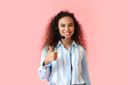 African-American consultant of call center showing thumb-up on pink background