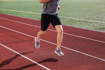 Obraz premium Athletic man running on red track with green field, fitness and healthy lifestyle training, outdoor exercise and sports activity
