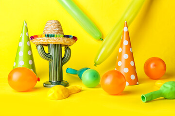 Balloons with party hats and cactus toy on color background