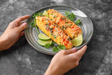 Woman holding plate with tasty Elote Mexican Street Corn on black background
