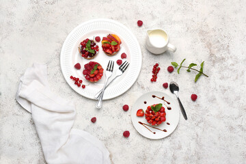 Plates with tasty berry tartlets on grunge background