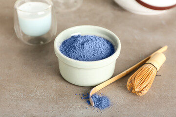 Bowl of powdered blue matcha tea, chasen and chashaku on grunge background