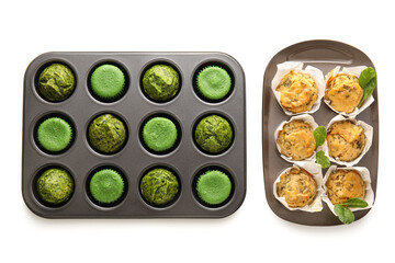 Baking tins with tasty spinach muffins on white background