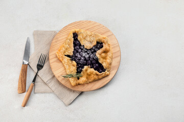 Board with tasty blueberry galette on light background
