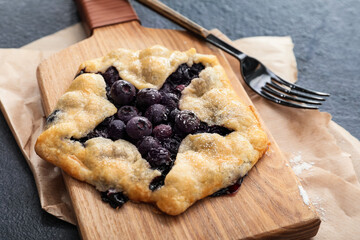 Board with tasty blueberry galette on dark background, closeup