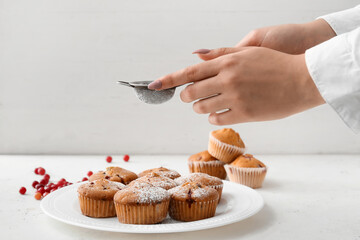 Woman sprinkling sugar powder onto delicious cranberry muffins on table
