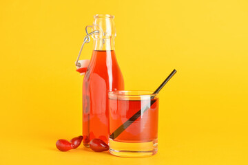 Glass and bottle of healthy dogwood berry drink on color background
