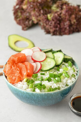 Tasty poke bowl with salmon and vegetables on light background