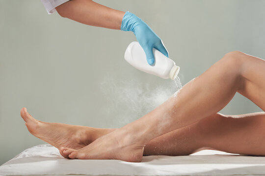 Cosmetologist is sprinkling and distributing talcum powder on a young girl's leg before the epilation procedure. The girl is lying on a couch in a beauty salon, she does the procedure shugaring