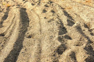 A deep rut and footprints on a sandy road. Sand pattern and texture.