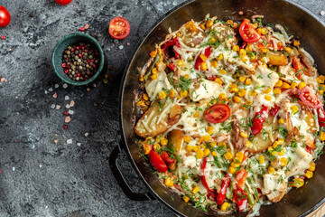 Fried potatoes with onions, corn, tomatoes, bacon and cheese on the rustic kitchen table. Top view