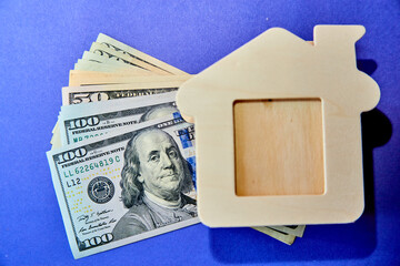 concept - the mock-up of a wooden house lies on a stack of money on a purple background