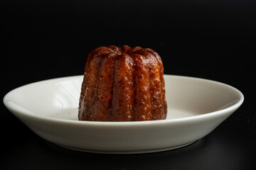 A piece of canelé on the dish with black background