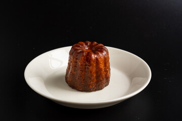 A piece of canelé on the dish with black background