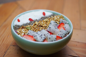 granola yoghurt bowl with cereal, strawberry, pitaya,  coconut flake and lycium chinense on wooden table