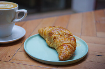 curved french croissant in cyan ceramic plate and cup of coffee with rosetta pattern latte art on wood table