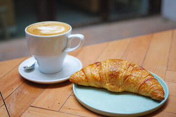 Curved French Croissant in cyan ceramic plate and cup of coffee with rosetta pattern latte art on wooden table