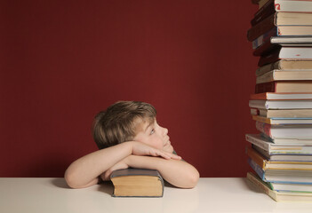 Back to school. Boy with books at a white table on a red background