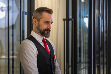 Senior caucasian waiter in formal waistcoat uniform is waiting to greet the customers in front the restaurant