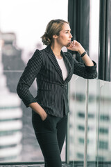 Young business woman looking out the window thinking about her project. She is dressed in black suit with white shirt inside.