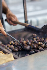Man roasting chestnuts at street stall using metal utensils