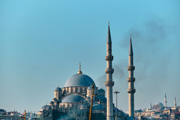 Fototapeta na wymiar Old ottoman mosques, selective focus of Yeni Mosque (yeni camii) and behind blurred Suleymaniye Mosque in istanbul, turkey, 03.03.2021 and smoke of transportation ferry with grain, blue sky background