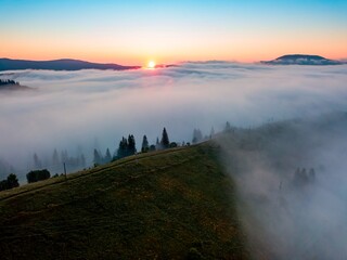 Fog spreads over the mountains at dawn. The sun rises on the horizon. Ukrainian Carpathians in the morning. Aerial drone view.