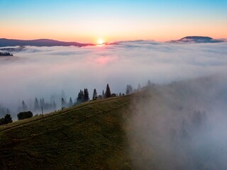 Fog spreads over the mountains at dawn. The sun rises on the horizon. Ukrainian Carpathians in the morning. Aerial drone view.