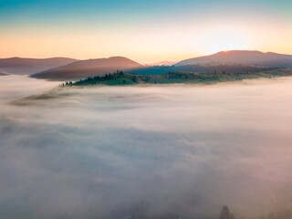 Fog spreads over the mountains at dawn. The sun rises on the horizon. Ukrainian Carpathians in the morning. Aerial drone view.