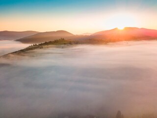 Fog spreads over the mountains at dawn. The sun rises on the horizon. Ukrainian Carpathians in the morning. Aerial drone view.