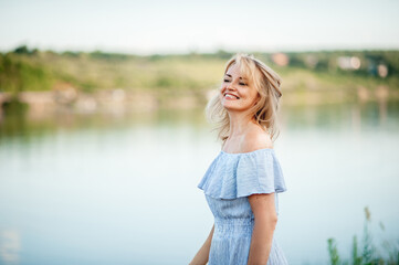 Fototapeta na wymiar A beautiful blonde woman smiles and laughs on a summer day by the water. Portrait close-up. The wind ruffles her hair. Happy and free woman about 40.