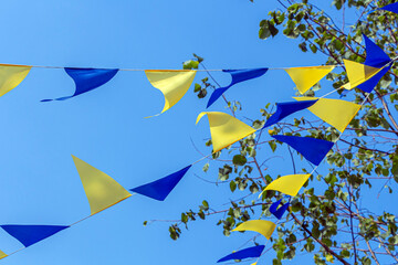Garlands with multicolored triangular holiday flags against blue sky at sunny day. Party flags decoration outdoors